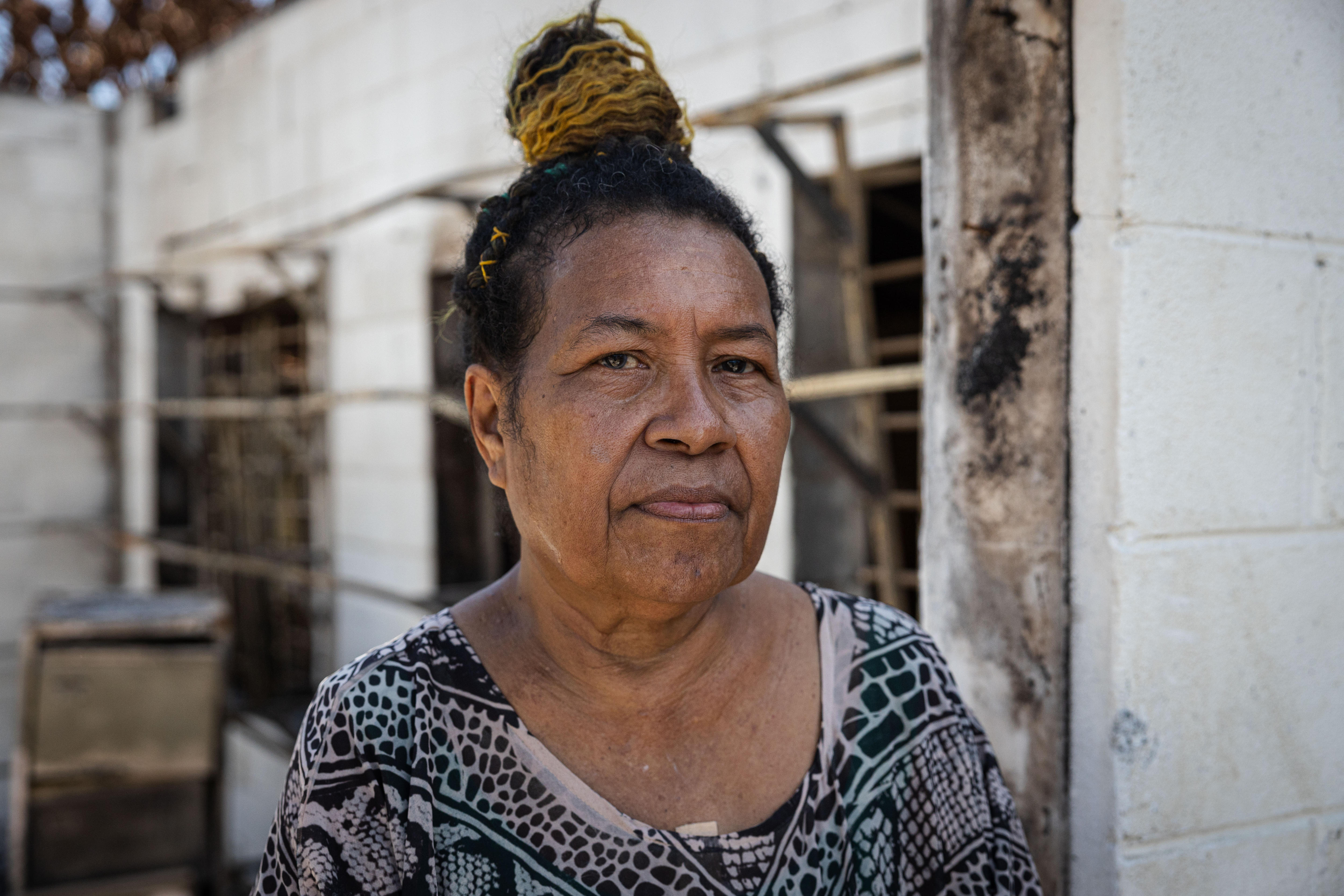 A woman stands in front of the shell of a building.