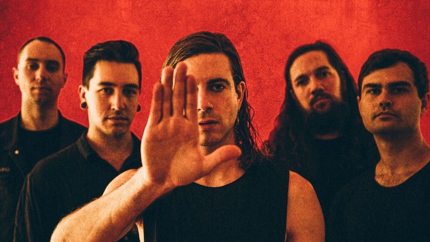 Press shot of In Hearts Wake; band dressed in black against burnt orange background