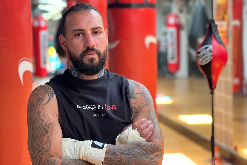 a boxer with his arms crossed standing in front of punching bags at a boxing studio