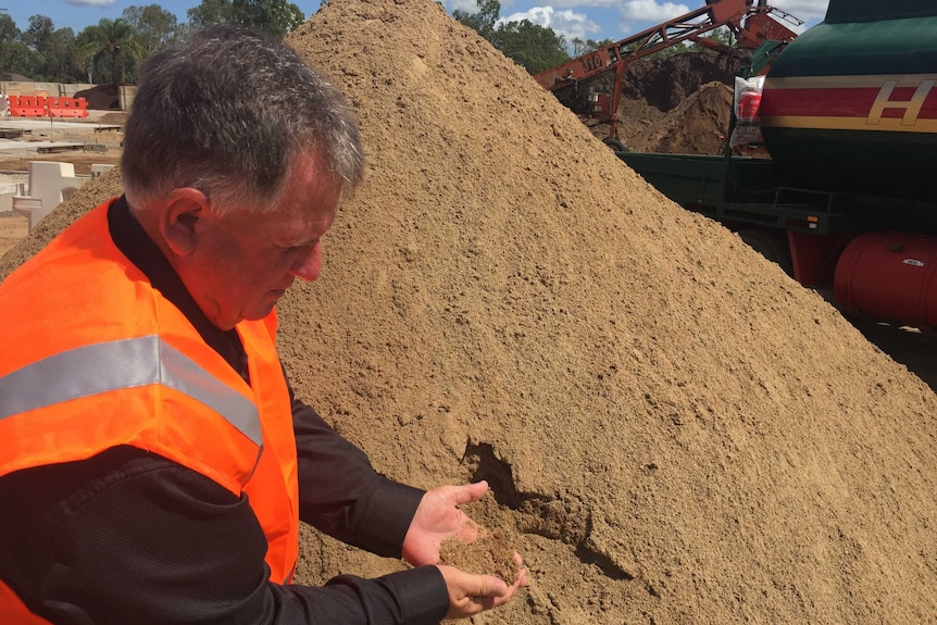 Rockhampton councillor Neil Fisher inspects construction sand.