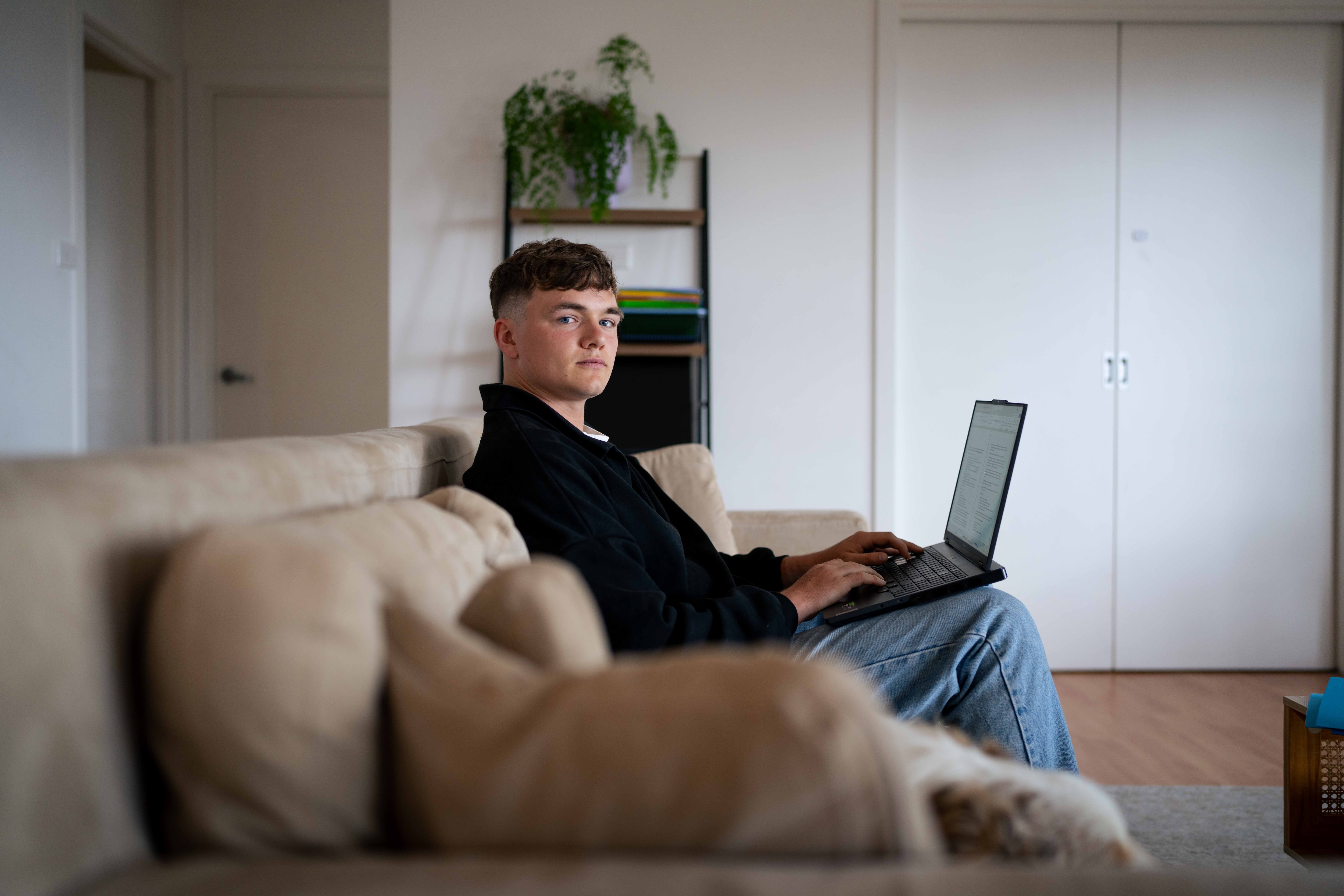 Man sits on couch with a laptop resting on his lap, posing for photo