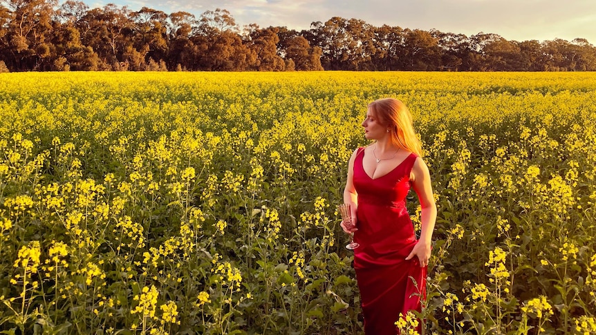 A young woman in a red dress stands in a field of yellow flowers.
