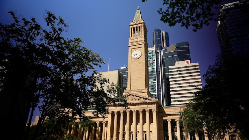 A wide shot of the Brisbane city hall among trees.