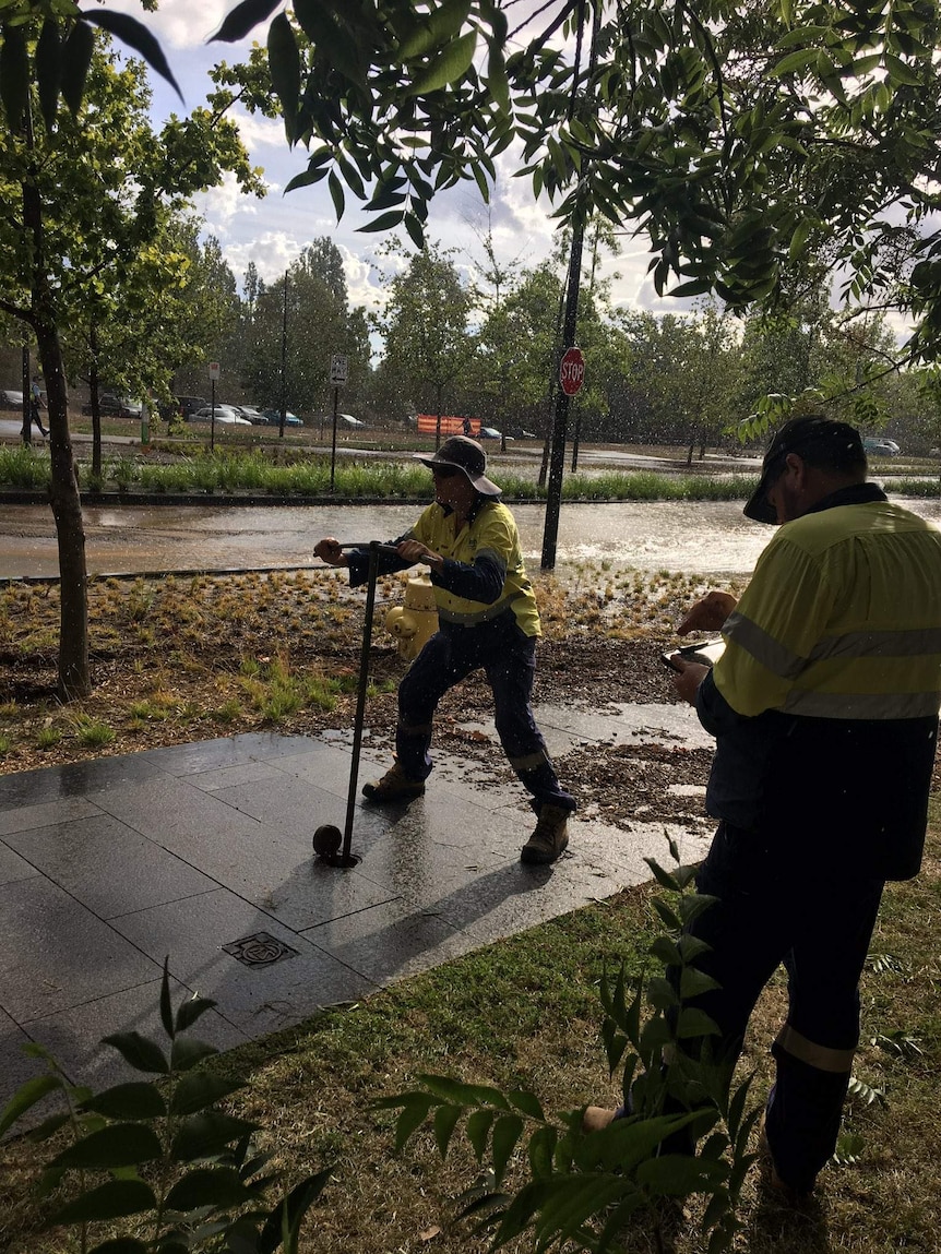 Crews work to stop the flow of water after a burst main flooded Constitution Avenue in Canberra.