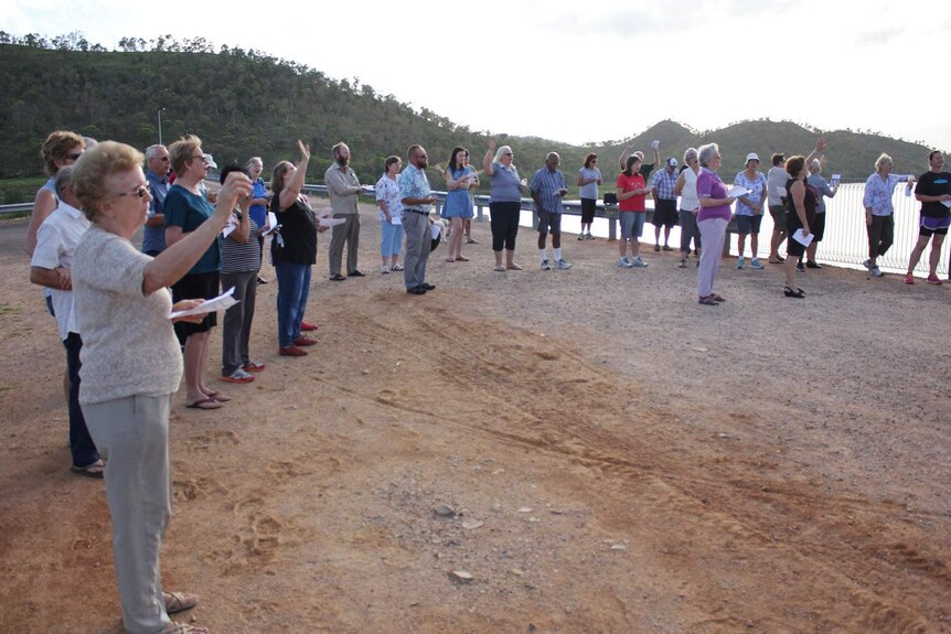 A group of people gathered at Ross River Dam in Townsville raise their arms in prayer.