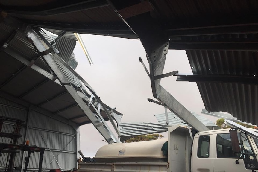 A hole in the shed roof, taken from inside the collapsed shed, pieces of twisted metal skewering the truck inside.