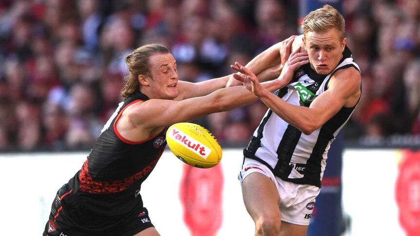 An AFL player pushes another AFL player with both hands as they contest for the mid-air ball.