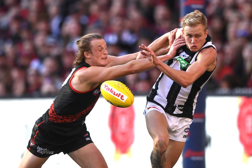 An AFL player pushes another AFL player with both hands as they contest for the mid-air ball.