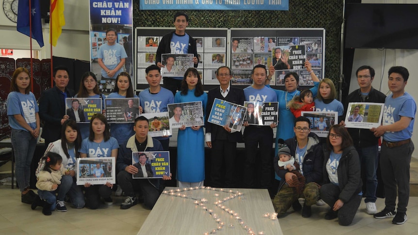 People stand holding signs and wearing blue in front of an outline of Vietnam in candles.