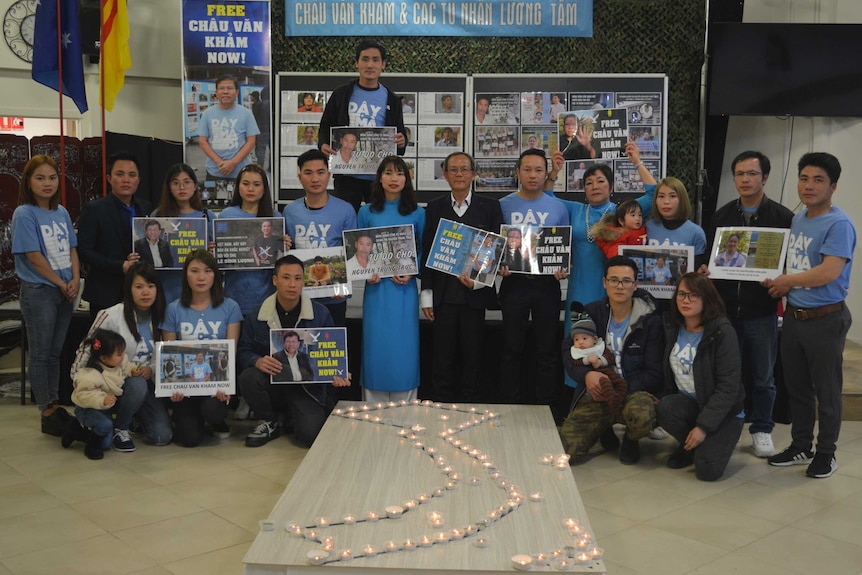 People stand holding signs and wearing blue in front of an outline of Vietnam in candles.