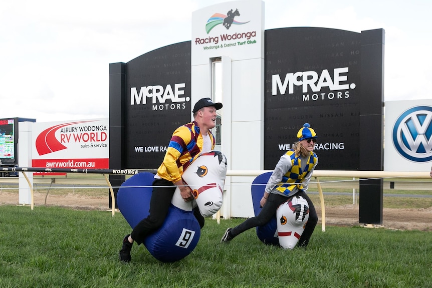 Two men in jockey silks bounce on blow up ponies towards a finish line at a race track