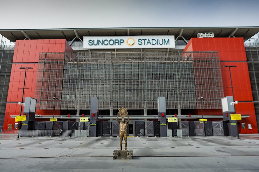 A wide shot of Suncorp Stadium. A bronze statue of WAlly Lewis lifting a trophy in the foreground. 
