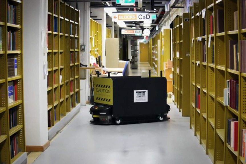 An old Automated Guided Vehicle is moving through library stacks.