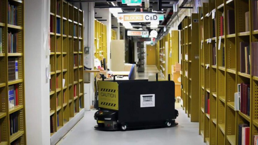 An old Automated Guided Vehicle is moving through library stacks.