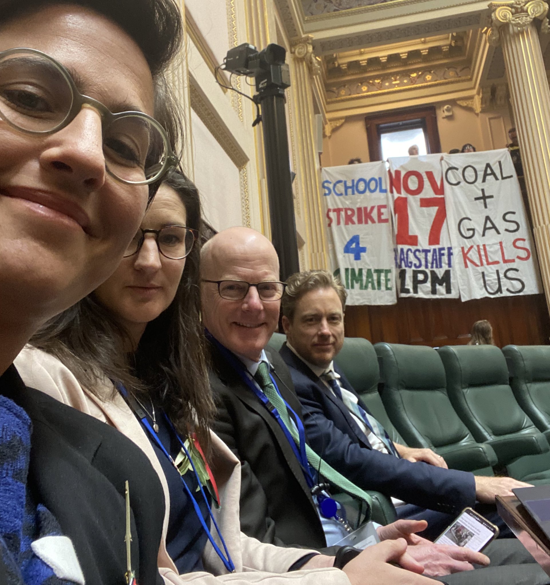 Gabrielle de Vietri and three of her colleagues sitting in the lower house, behind them are three climate change banners.