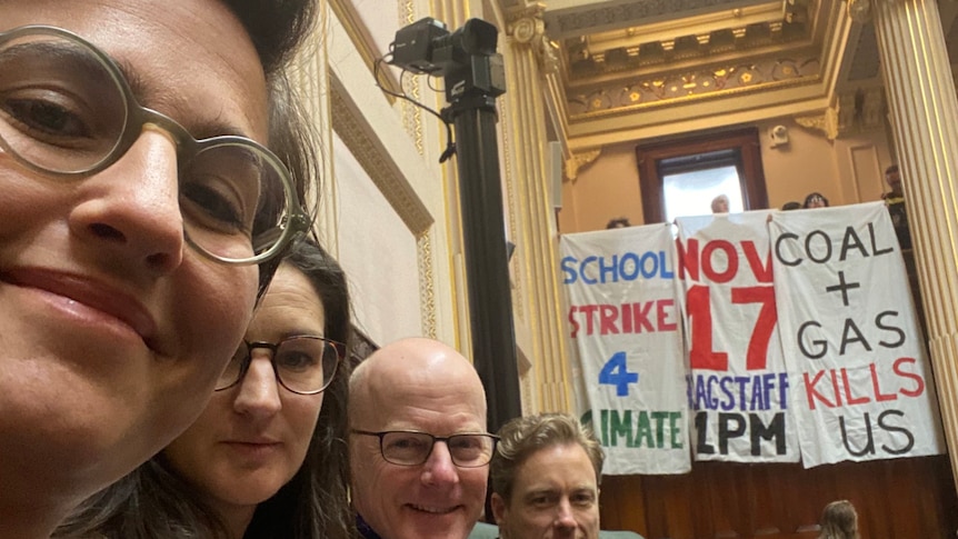 Gabrielle de Vietri and three of her colleagues sitting in the lower house, behind them are three climate change banners.