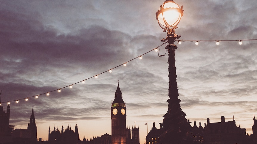 A photo of an old fashioned street lamp at dusk with big ben in the background.