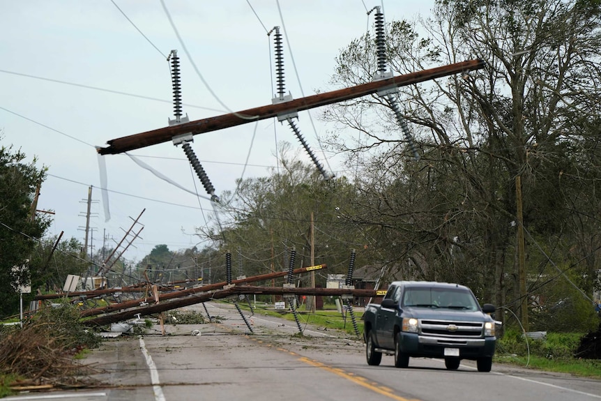 Power lines and debris lay across a cracked highway as a sports utility vehicle drives by.