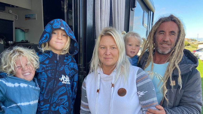 A couple with fair hair and their three children outside a caravan