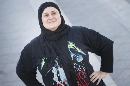 A woman in a headscarf and a t-shirt stands with her hands on her hips smiling