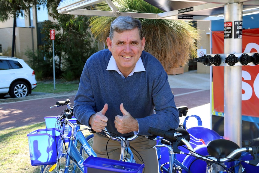 Ken Travers giving the thumbs up while leaning on an Urbi bike.