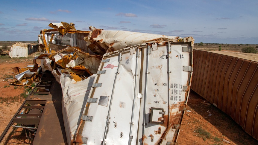 A badly damaged freight container pushed sideways half-off its train flatbed.