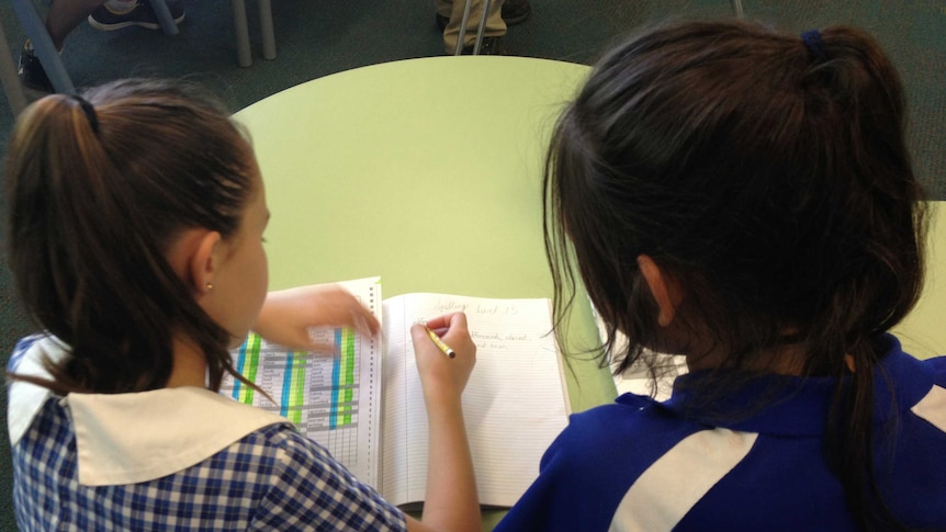two school girls write in a book during class.