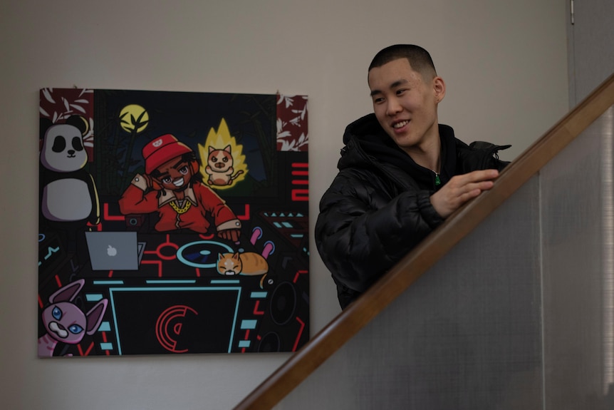 一名短发的中国年轻男子站在一幅画旁的楼梯上。