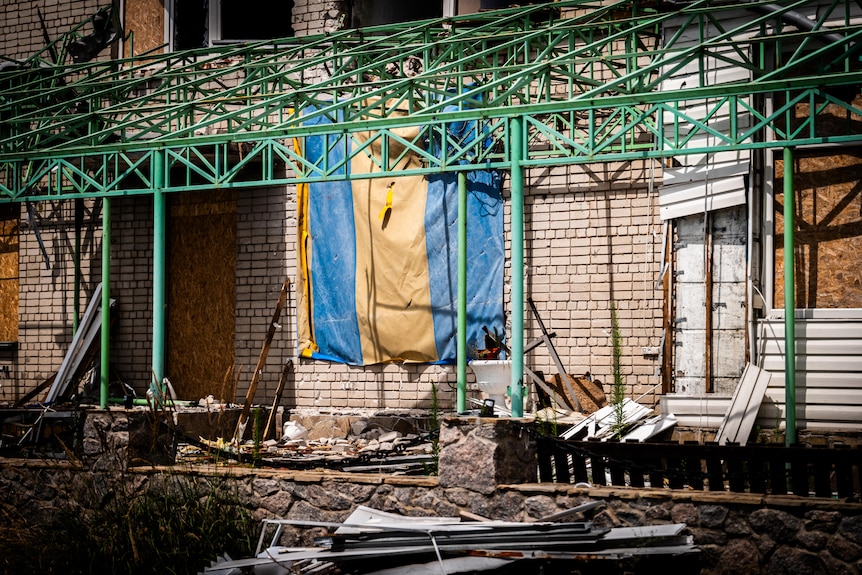 Green metal scaffolding is set up outside a damaged building, a flag with Ukraine's yellow and blue fixed to the brick wall