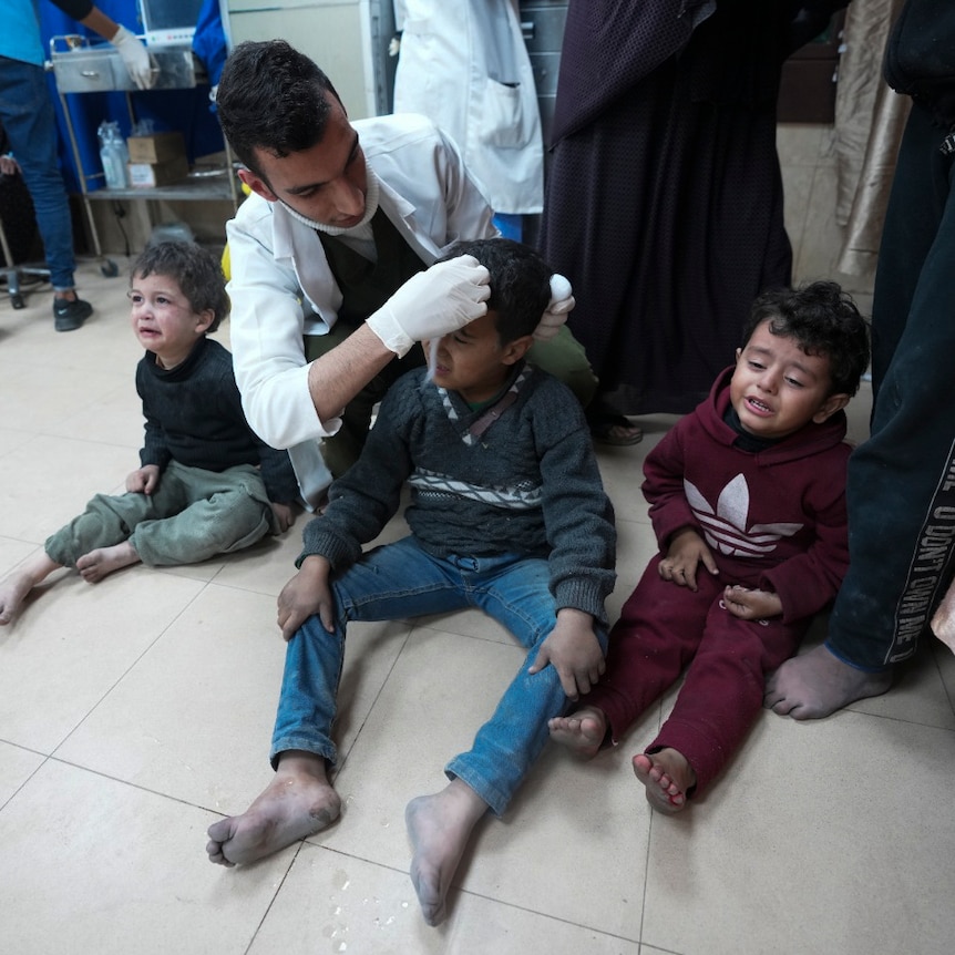 Doctor treats three crying kids on the floor 