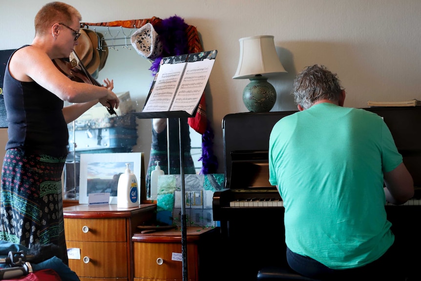 Steph plays a violin in front of sheet music, while Michael plays piano in a green shirt.