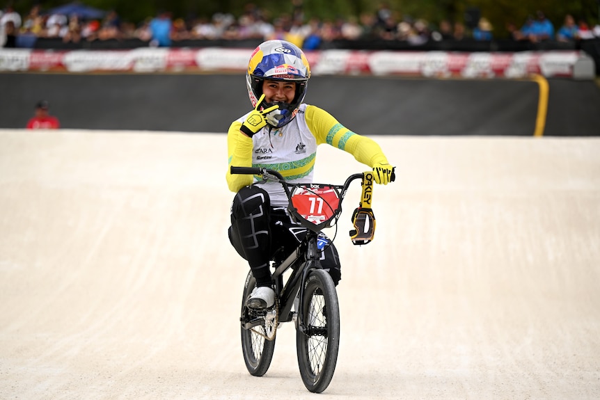 Saya Sakakibara smiles and holds up two fingers while on the bike