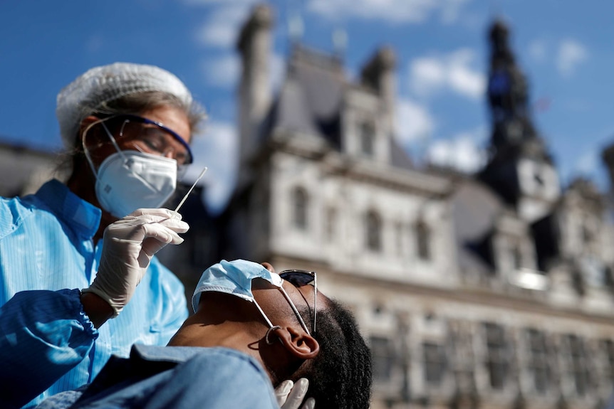 A health worker in PPE holds a swab above a man's face