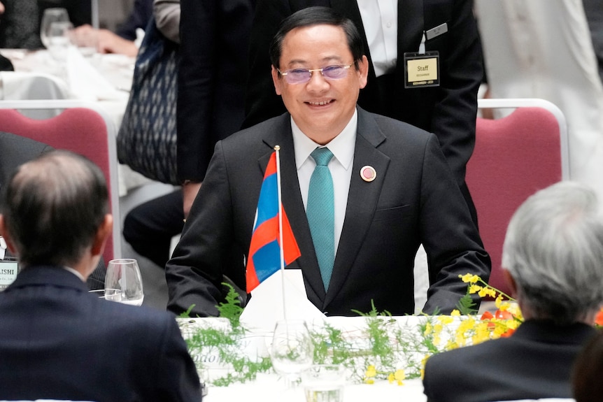Laos' Prime Minister Sonexay Siphandone smiles as he sits at a table during a meeting in Tokyo in a suit and tie