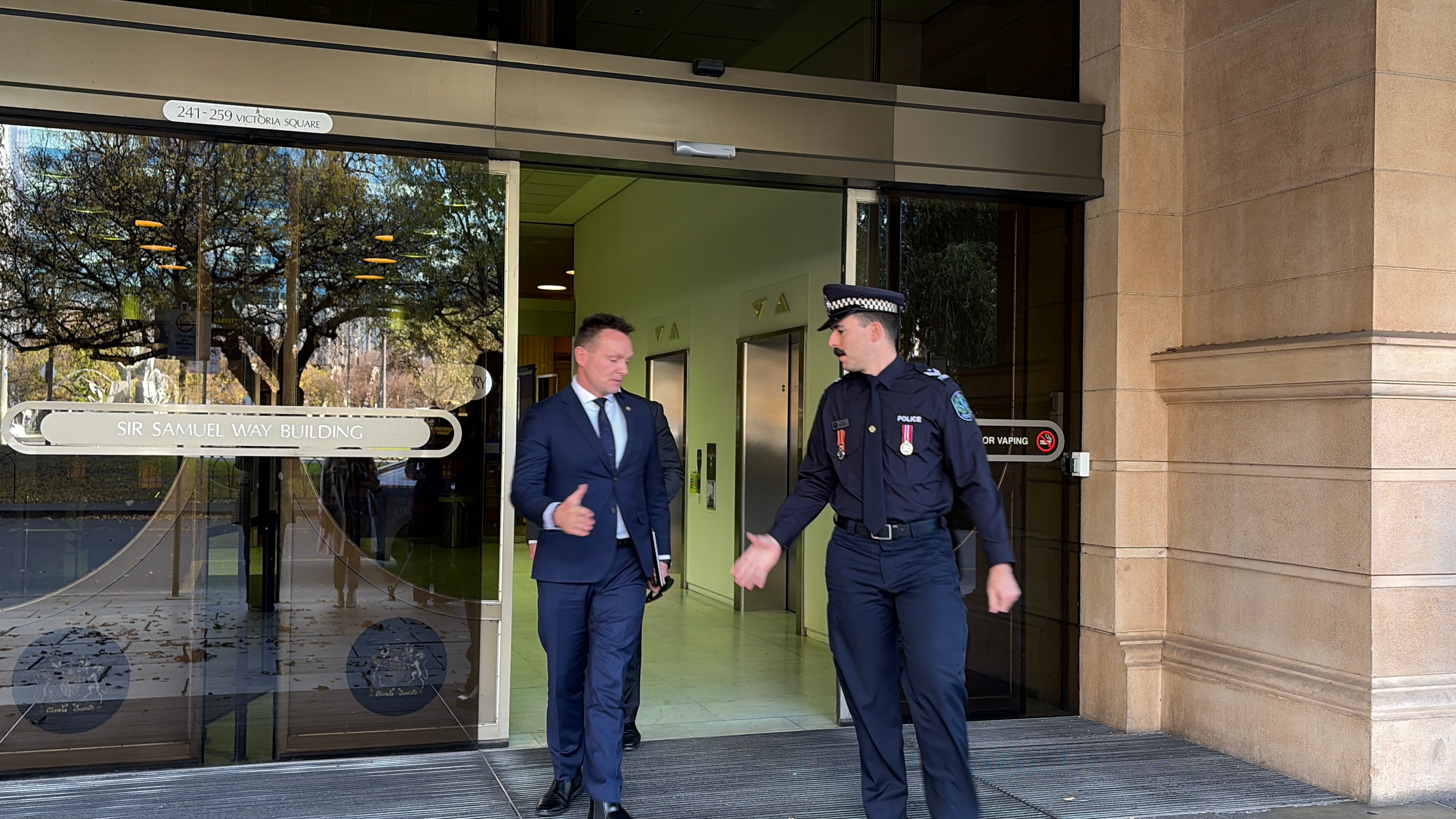 A man in a blue suit shakes hands with a police officer outside a building.