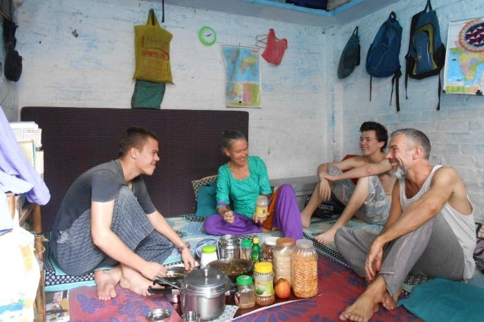 Two young adult men, one man with facial hair and one lady with hair pulled back sit in a small room in slum area.