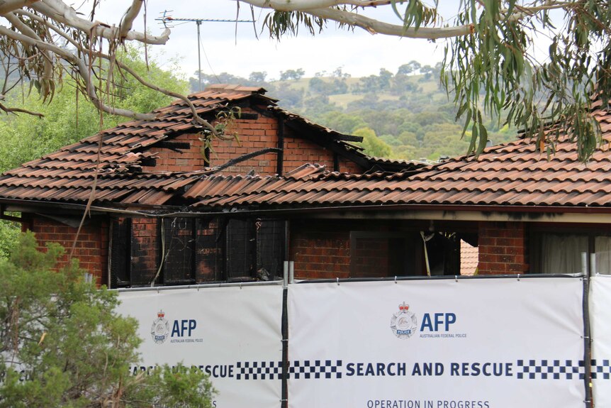 A police barrier in front of a burnt-out house.