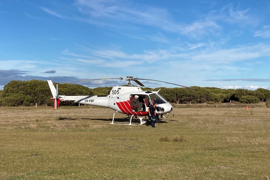 A helicopter in a field with two people disembarking 
