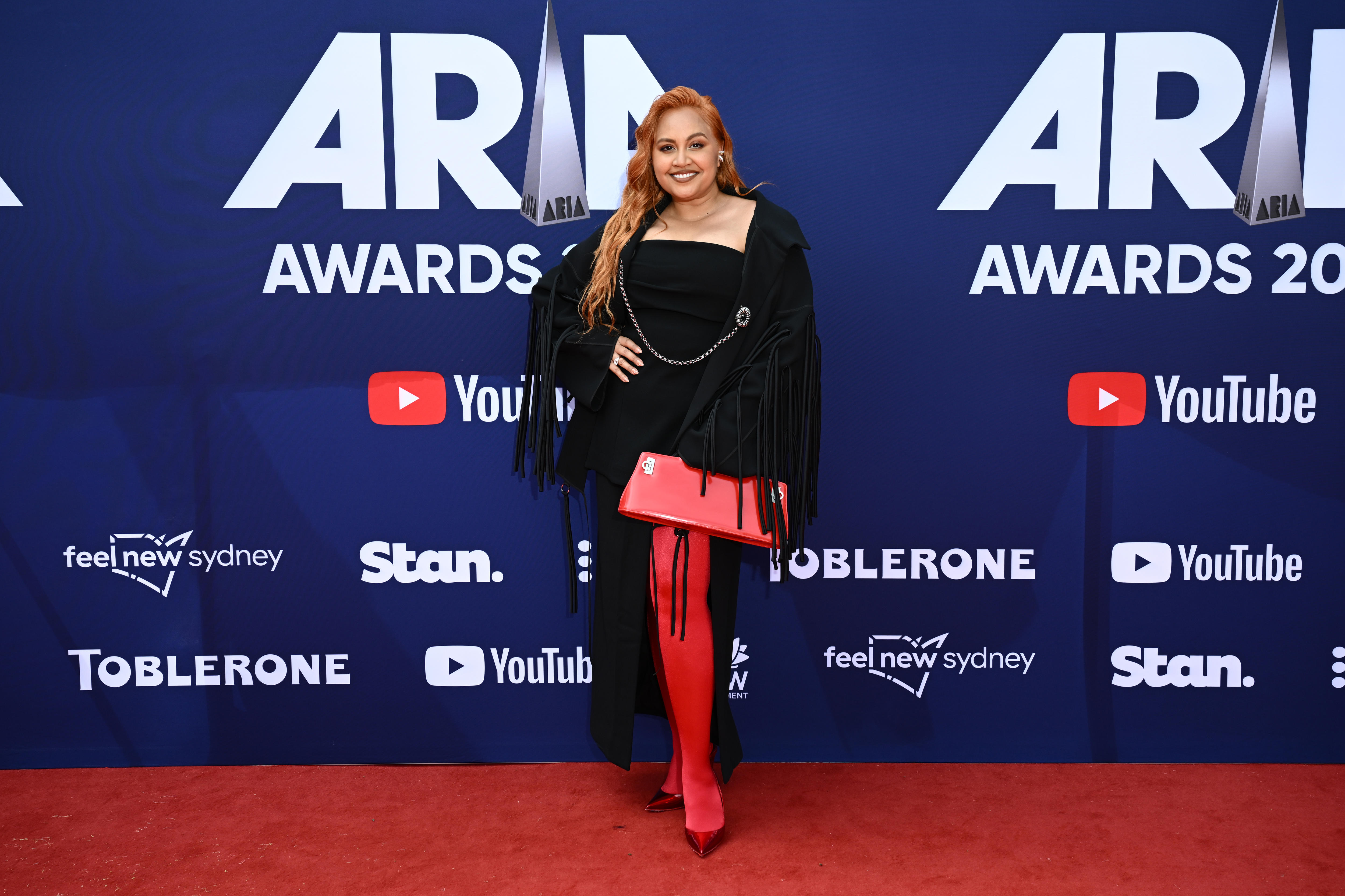 A lady wearing a black dress with red stocking and a red bag