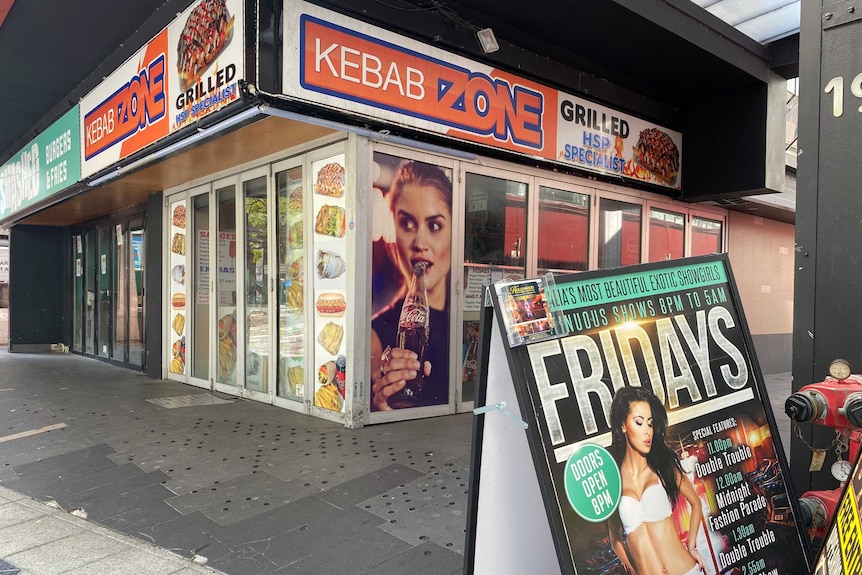 A picture of a closed Kebab shop called Kebab Zone with a billboard for a strip club in the foreground
