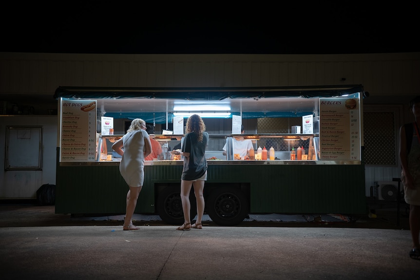 Two women visit a burger stand that is poorly lit