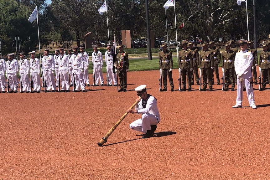A man in uniform crouches down playing the didgeridoo at the Australian War Memorial.