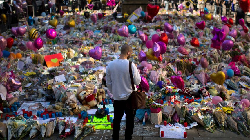 A man stands in front of an array of flowers in central Manchester, left in memory of the victims.