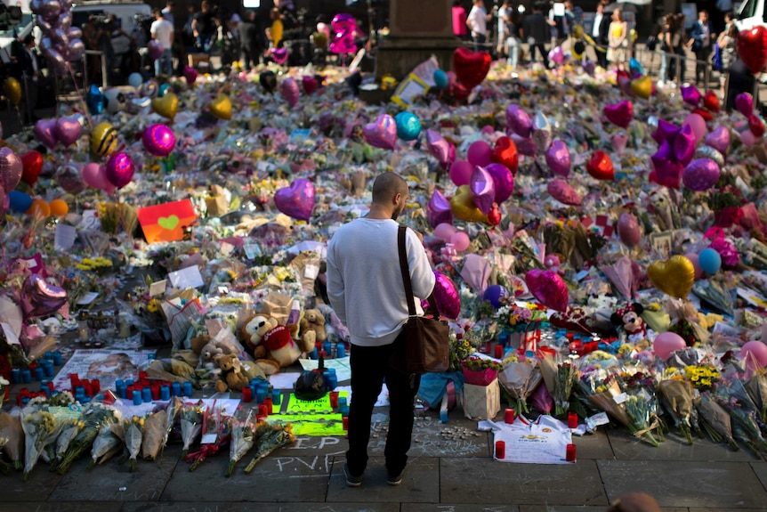 A man stands in front of an array of flowers in central Manchester, left in memory of the victims.