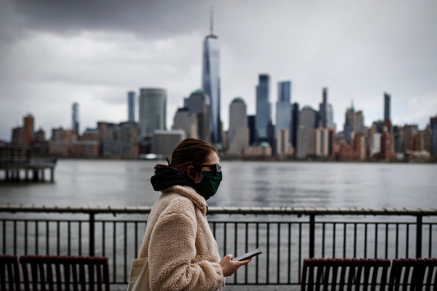 The downtown New York City skyline looms over pedestrians wearing masks due to COVID-19 concerns.
