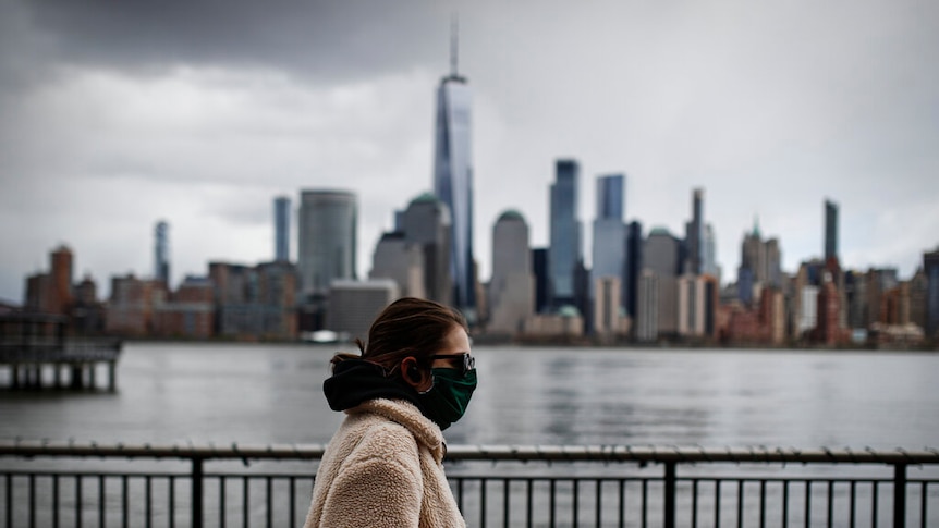 The downtown New York City skyline looms over pedestrians wearing masks due to COVID-19 concerns.