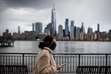 The downtown New York City skyline looms over pedestrians wearing masks due to COVID-19 concerns.