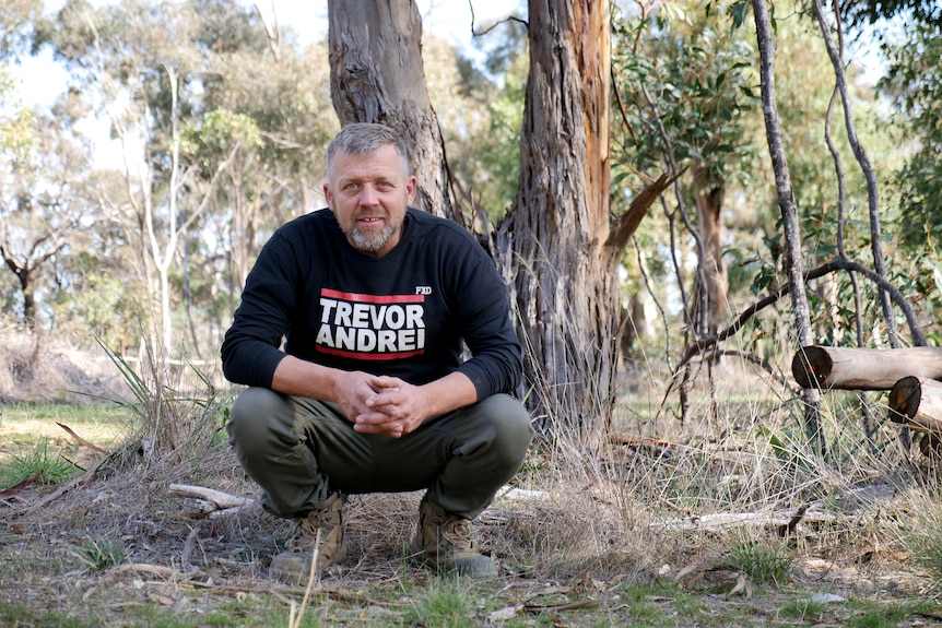 Trevor Andrei stands in a short with his name on the front at his property in regional Victoria on a summer day