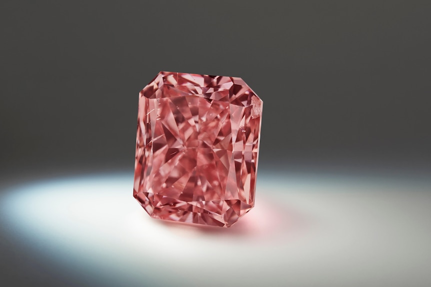 A beautiful, radiant-cut oblong dark pink diamond is spotlit from the left in a dark space.