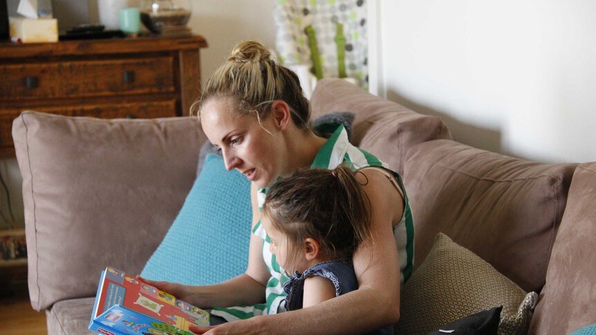 A woman reading a book to a young girl in a living room